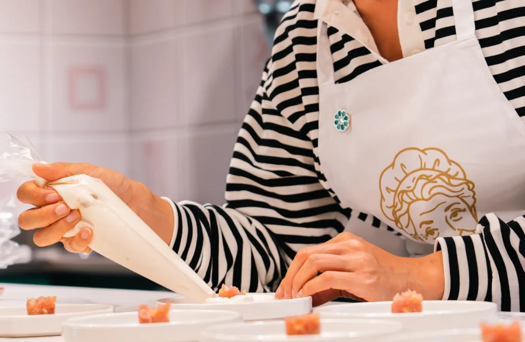 margherita_cooking_class-shoot_01-orizzontale-13 Persona impegnata nella preparazione e decorazione di piccoli piatti, con attenzione ai dettagli e alla presentazione delle portate.